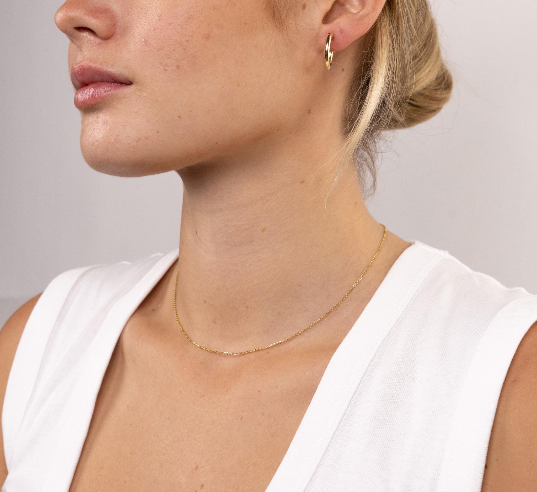 Close-up of a person wearing a gold necklace and earring on a plain background