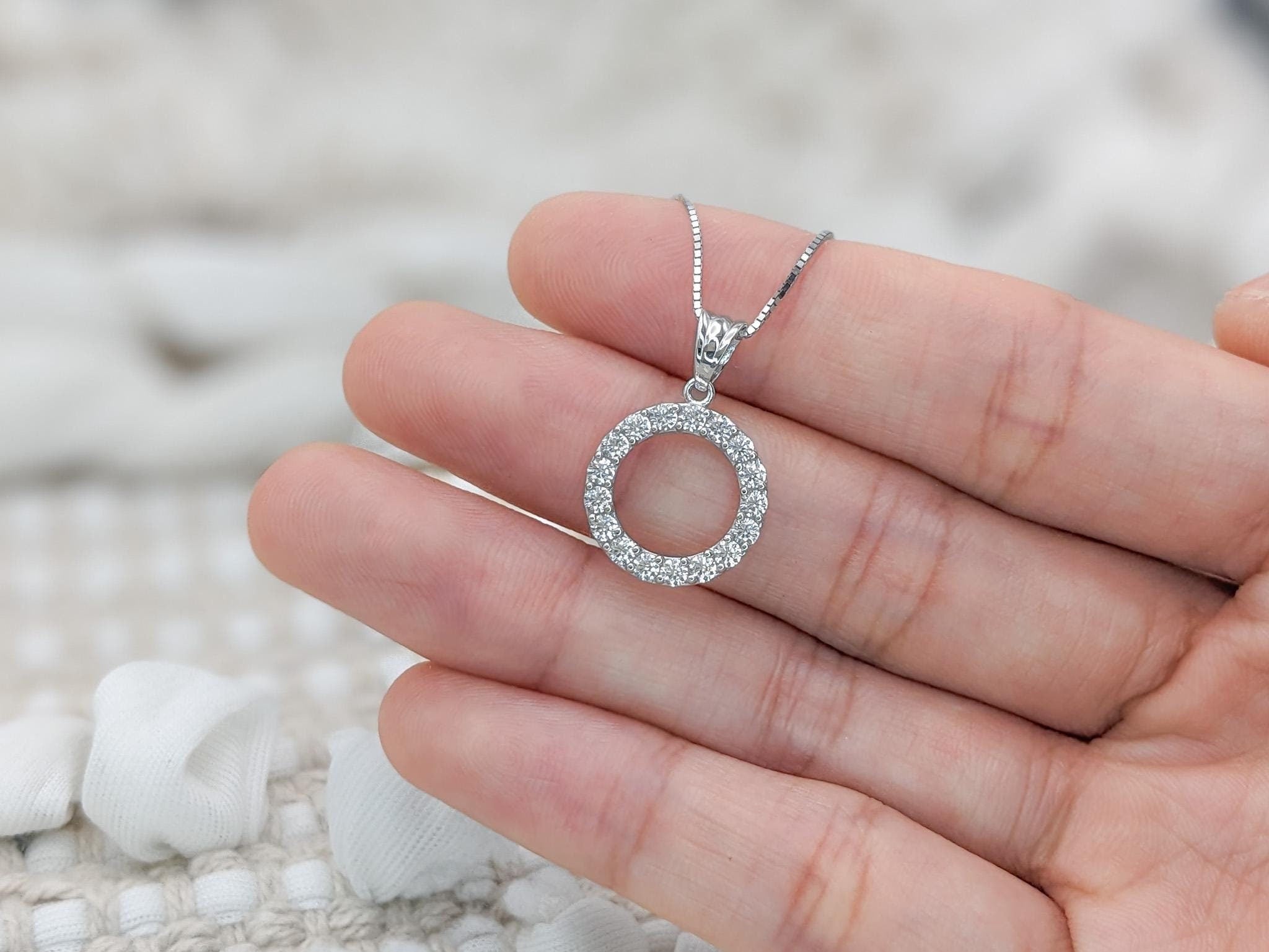 May include: A silver necklace with a round pendant encrusted with small, clear gemstones.