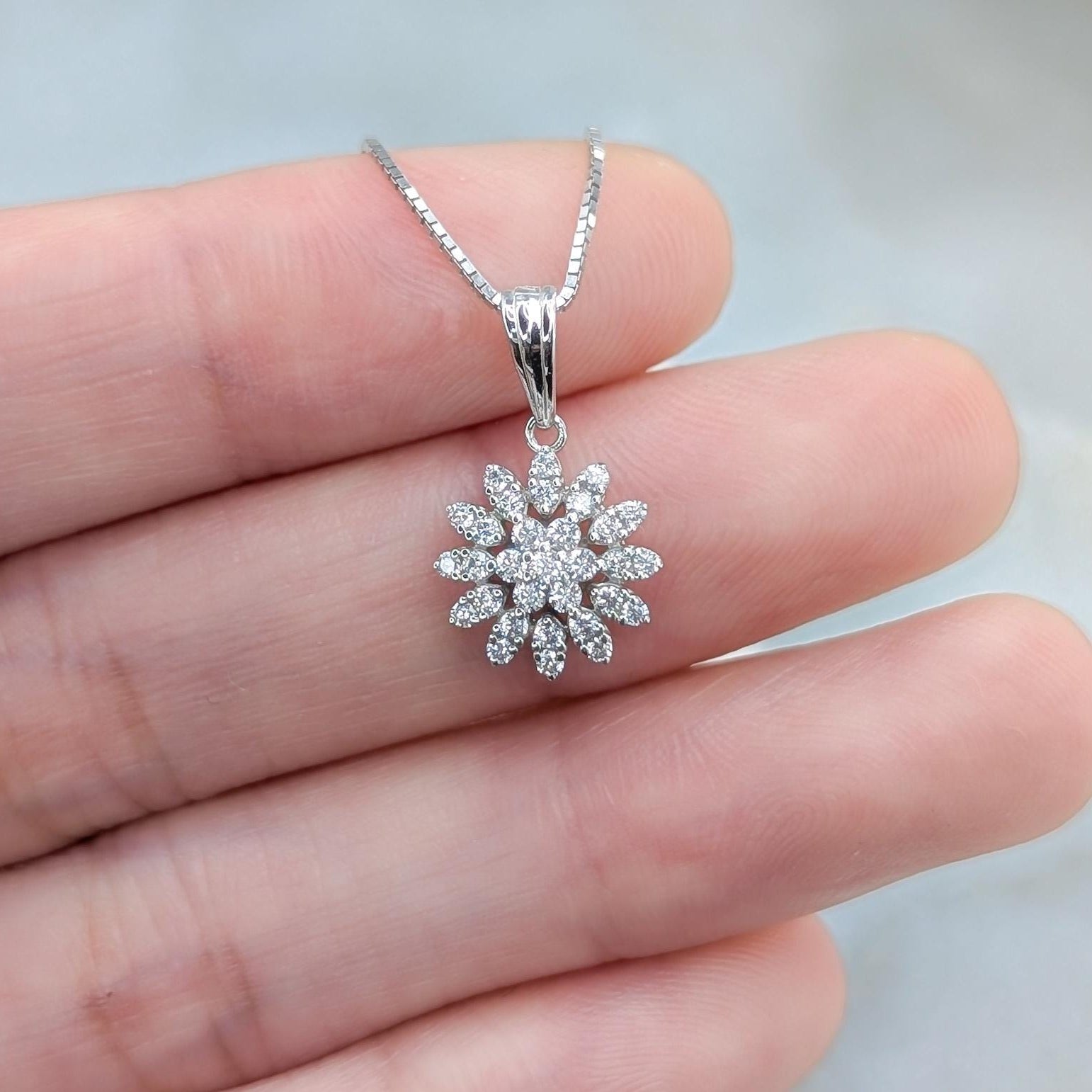 May include: A silver snowflake pendant necklace with a chain. The snowflake is made of small, clear stones.
