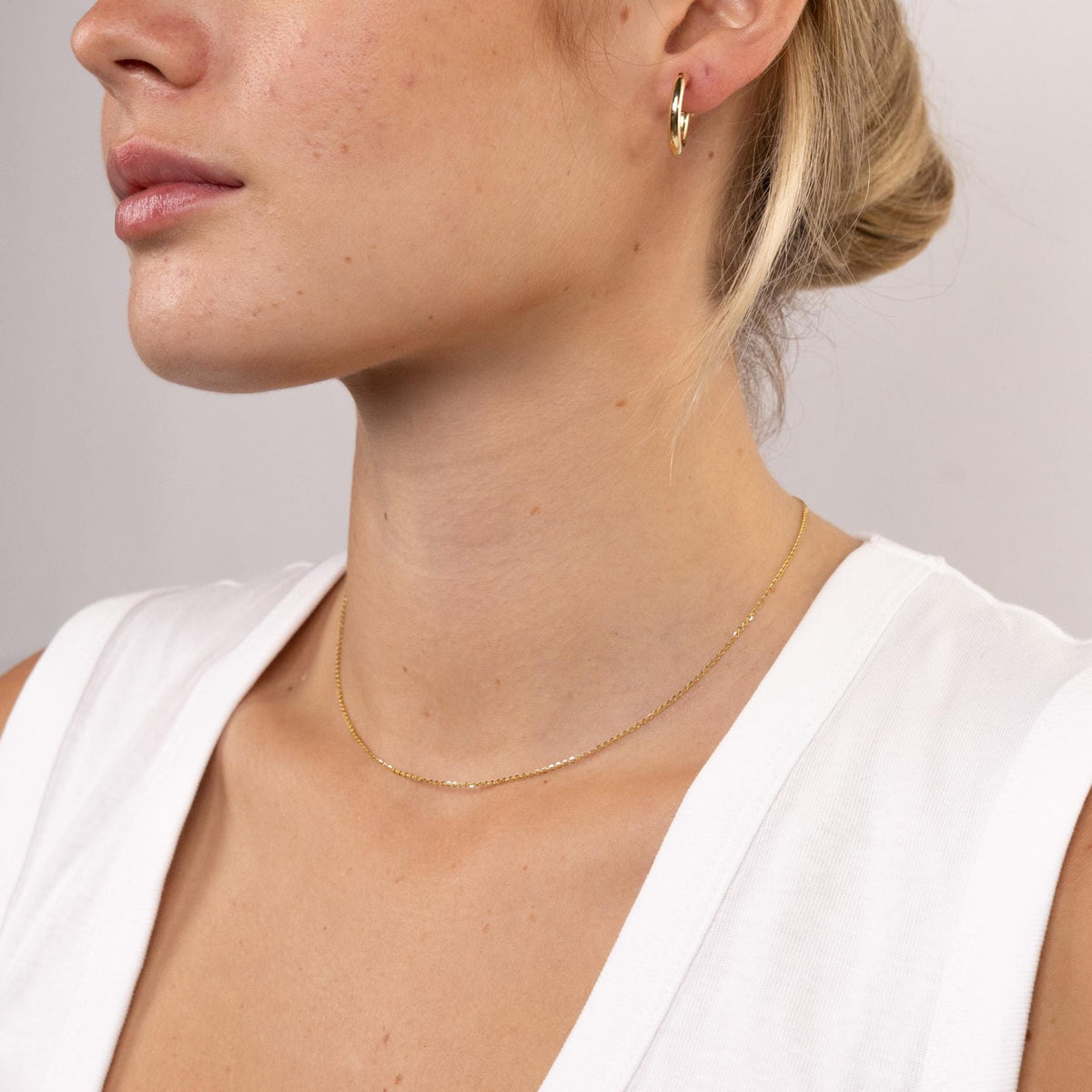 Close-up of a person wearing a gold necklace and earring on a plain background