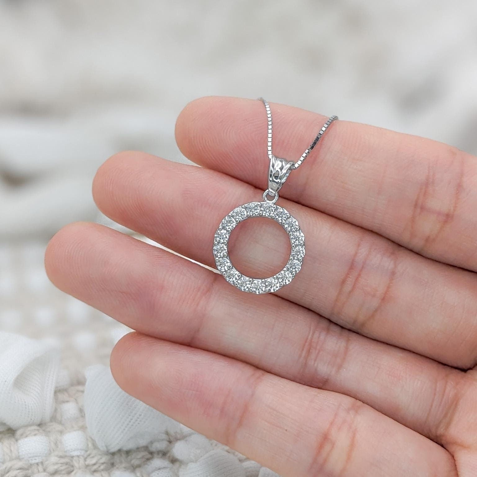 May include: A silver necklace with a round pendant encrusted with small, clear gemstones.